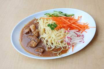 Spaghetti with steamed pork and vegetable on white plate against wooden background
