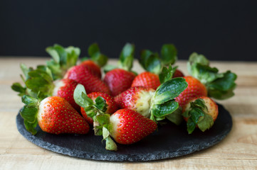 Black slate board with fresh strawberry on wooden table, selective focus