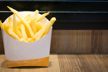 Close up french fries in a white paper on the brown table.