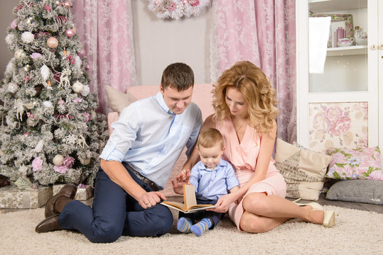 happy parents with toddler boy read the book in Christmas