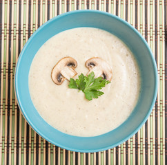 Mushroom cream soup with potatoes on blue bowl on a wooden table, top view
