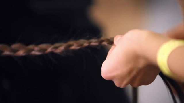 Hairdresser makes hairstyle for the model close-up. Preparing for the fashion show. Dressing room for models. Weaving hair braids.