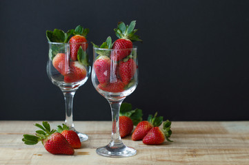 Background with big strawberries in vine glasses on wooden table near black wall. Healthy dessert. Romantic eating
