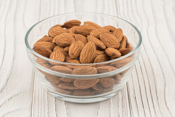 Almonds in a glass bowl on white old wooden table.