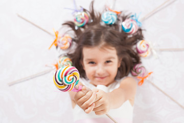 Pretty girl among the sweets, candies and lollipops. Funny child with candy lollipop, happy little girl eating big sugar lollipop, kid eat sweets. surprised child with candy. 