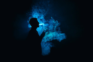 The man smoke an electric cigarette against the background of the blue light