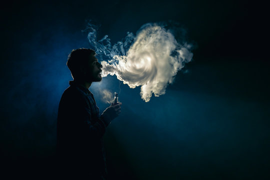 The man smoke an electronic cigarette on the background of the bright light