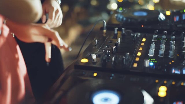 Hands of DJ tweak various track controls on dj's deck in 4K