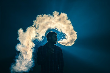 The man smoke an electronic cigarette on the background of the bright light
