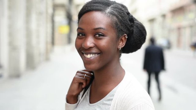 Young beautiful black woman outdoor in the city, looking at camera smiling - happiness, carefree, serene concept