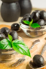 Foto op Plexiglas Black olives with green leaves on a wooden background © romensky