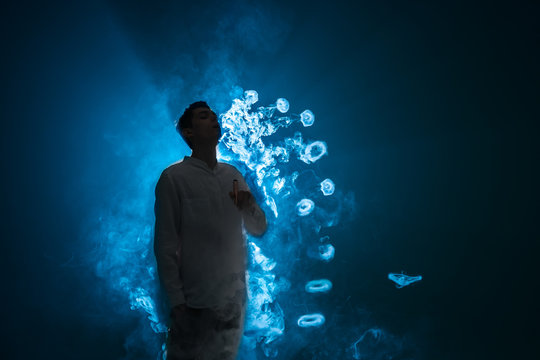 The man smoke an electric cigarette with a ring against the background of the blue light