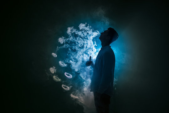 The man smoke an electronic cigarette with a ring against the background of the blue light