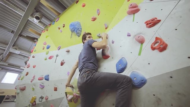 Young fit man climber on artificial climbing wall rock in bouldering gym