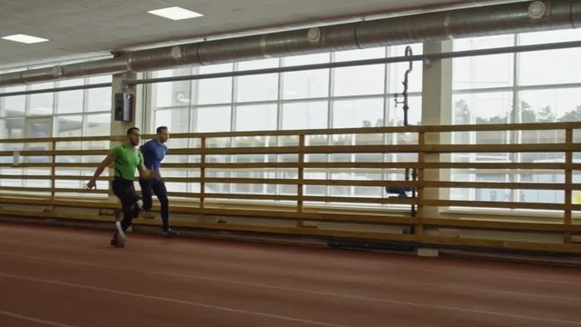 Slow motion shot of professional athlete with two whole legs competing with amputee runner with artificial limb on stadium track