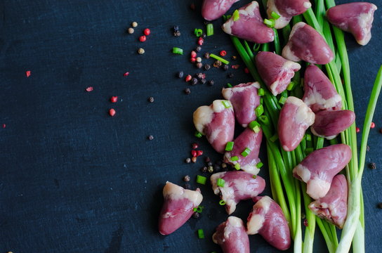 Raw chicken hearts with green fresh spring onion on black slate stone background