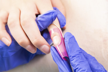Manicure specialist care by finger nail in beauty salon. Manicurist uses professional manicure...