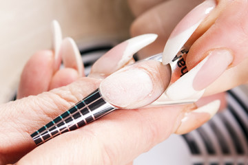 Manicure specialist care by finger nail in beauty salon. Manicurist uses professional manicure tool.  Use of a template (schablon) for acrylic nails