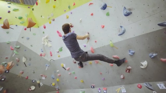 Free climber strong man on artificial climbing wall rock in bouldering gym