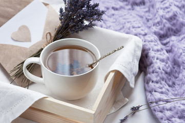 Un plateau avec une tasse de thé chaud et une lettre d& 39 amour à la lavande au lit avec une couverture tricotée