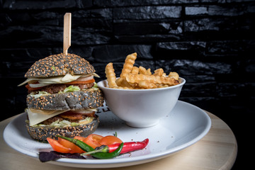 Delicious black burger with spices with fried potatos on a dark background