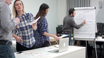 Male manager presenting pie chart on flipboard to his colleagues