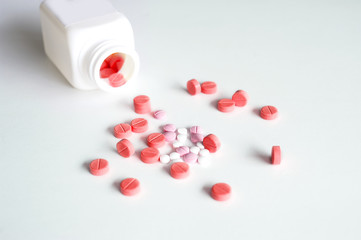Medical red, pink and white pills with plastic white bottle on white background