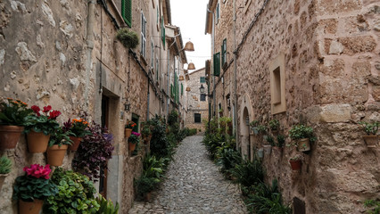 empty narrow street in Valldemossa Mallorca with typical historic houses on both sides and mountains in far distant background