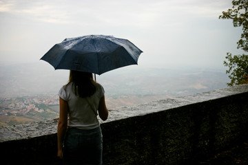 The girl under an umbrella looking over the valley in a rainy day.