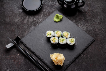 Japanese cuisine. Avocado sushi (maki) on a stone plate and dark concrete background.