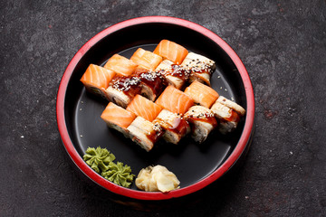 Japanese cuisine. Sushi roll set on a round wooden plate and dark concrete background.