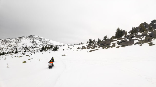 Men on snowmobile ride each other on the rocky slope.
