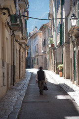 person walking along empty narrow street in town in Majorca with typical historic houses on both sides and mountains in far distant background