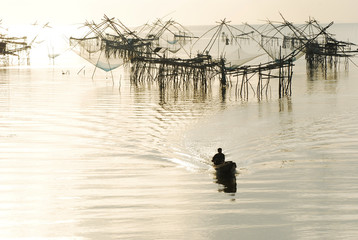 Fisherman sailing boat to the giant fishing nets in the sea on sun rise.