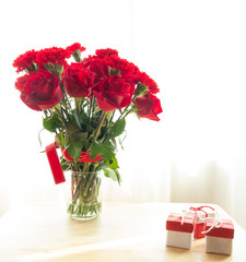 bouquet of red roses and red ribbon with present on wood table