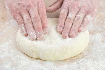 Pizza baking , starting to stretching dough on floured wooden board