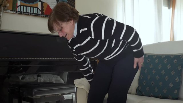 elderly woman with back pain gets up laboriously from the couch