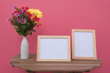 Two photo Frame on a wooden and Flowers in jar on pink background .