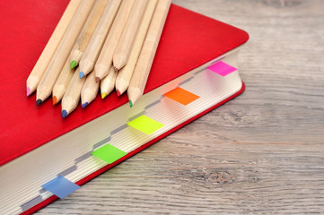 Obraz premium Red diary notebook and colored pencils on the desk wood texture.