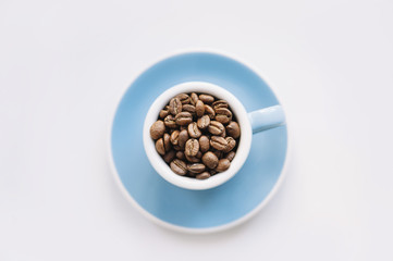 macro view of a blue espresso cup filled with freshly roasted coffee beans on a white background