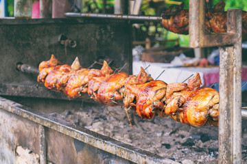 Free range chicken fire roasting traditional way on skewer at Thai old cafe background. Selective focus
