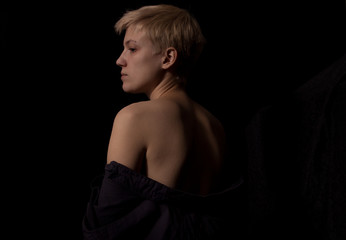 Attractive young Caucasian woman is sitting on a bed covered in shirt