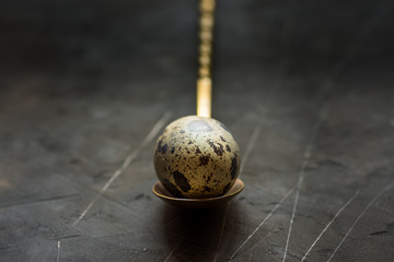 Quail egg on a  vintage copper spoon, close up, black scratched concrete background, Easter, minimalistic, moody, conceptual