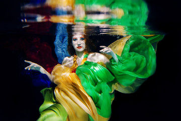 Red hair girl with big sea shell in colorful clothes on the dark background underwater