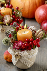 Floral arrangement with dry plants and candle in ceramic pot.