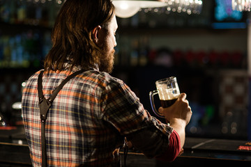 man sitting at the bar with a glass of beer in a shirt and braces 
