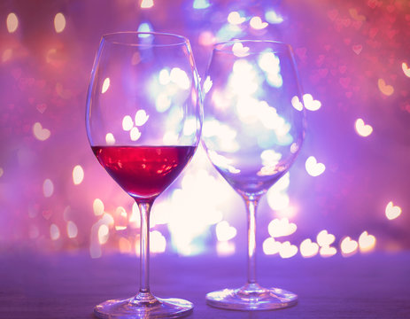 Two glasses with wine with hearts shaped bokeh background. St. Valentine's Day.