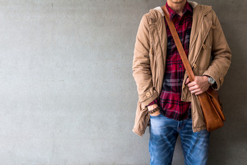 Men's casual outfits wear blue jeans with red plaid shirt, brown coat and leather bag standing over gray grunge background with space, lifestyle traveler, beauty and fashion concept

