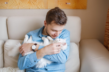 Attractive man in a blue shirt, playing with white fluffy cat - 134044299