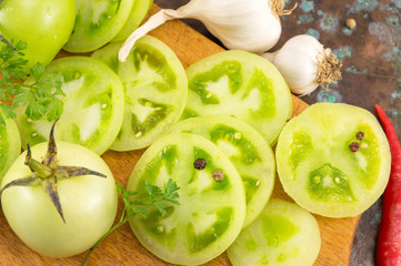 sliced green tomatoes with garlic and peppers on a wooden cuttin